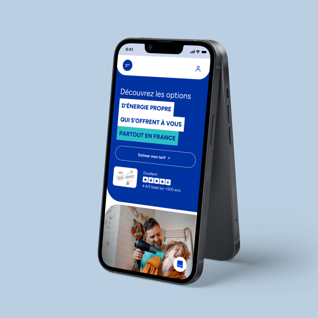 Un smartphone affiche l’écran d’accueil d’une application sur fond bleu clair. L’interface présente le message “Découvrez les options d’énergie propre qui s’offrent à vous partout en France”, un bouton “Estimer mon tarif”, une note d’excellence de 4,4/5 et une image floutée représentant une personne adulte et un enfant souriant dans une scène domestique.
